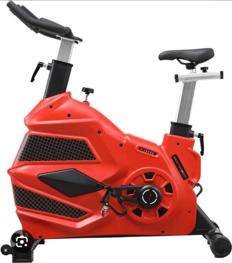 Large red commercial spinning fitness bike with a covered flywheel, side view — Electromart Uganda